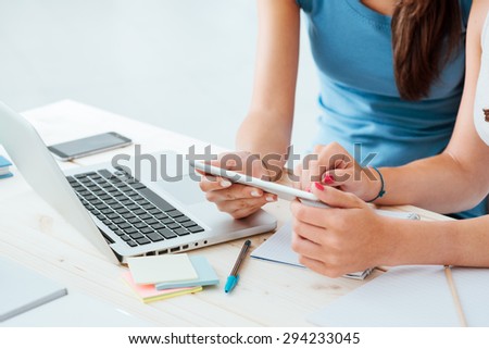 Teen girls sitting at desk and using a touch screen tablet, they are studying and using apps, hands close up