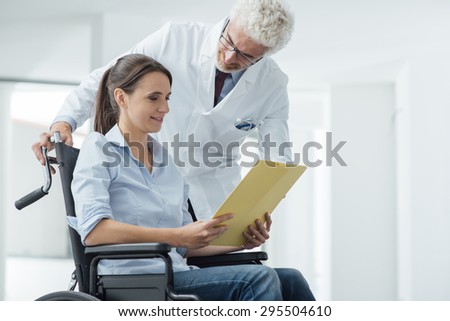 Doctor and patient examining a file with medical records, she is sitting on a wheelchair, assistance and health care concept