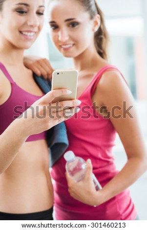 Happy young girls at the gym using a fitness app on a smart phone, technology and training concept