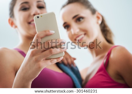 Happy young girls at the gym using a fitness app on a smart phone, technology and training concept