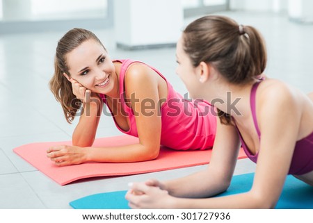 Cute girls at the gym lying belly down on a mat, talking and gossiping