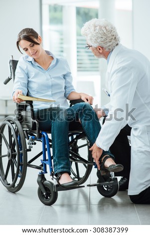 Doctor visiting an invalid woman in wheelchair, he is examining her leg, rehabilitation and physioteraphy concept