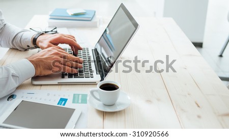Professional businessman working at office desk and typing on a laptop, unrecognizable person