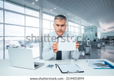 Frowning bank clerk at desk holding a sign and rejecting a loan application