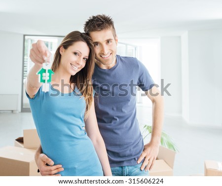 Young smiling couple holding their new house keys, real estate and relocation concept