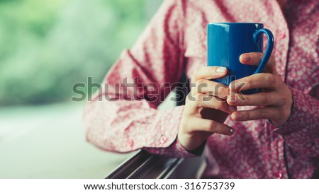 Woman at window holding a cup and having a relaxing coffee break, hands close up