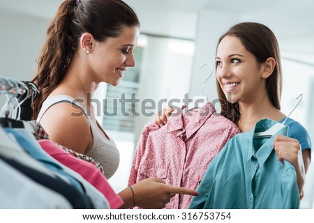 Girl shopping a choosing a shirt at the store, a young smiling sales clerk is helping her