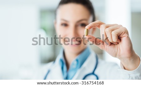 Smiling female pharmacist holding a pill, health care and prevention concept, hand close up