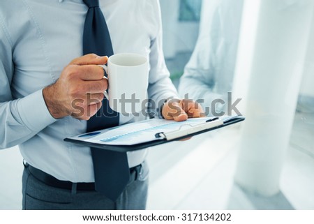 Executive working during his coffee break, he is holding a clipboard and a mug with coffee