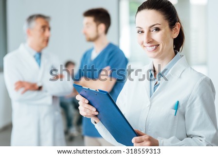Professional female doctor smiling at camera and posing, medical staff working on background, selective focus