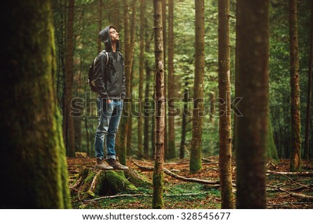 Hooded young man standing in the forest and exploring, freedom and nature concept