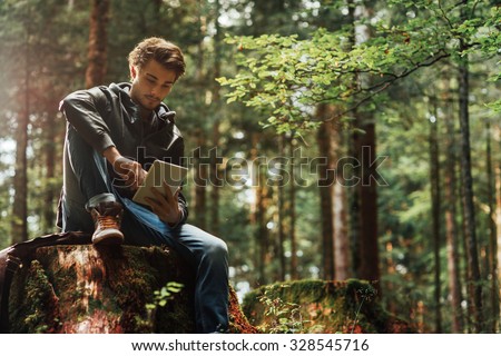 Young handsome man sitting in the woods and using a digital touch screen tablet, wi-fi connection and freedom concept