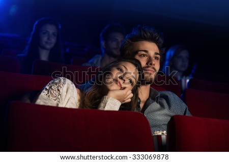 Young loving couple at the cinema watching a movie, he is hugging her girlfriend