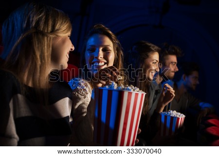 Group of teenager friends at the cinema watching a movie together and eating popcorn, entertainment and enjoyment concept