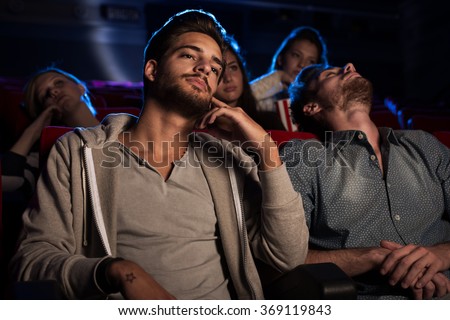Young people watching a boring movie at the cinema, one guy is sleeping