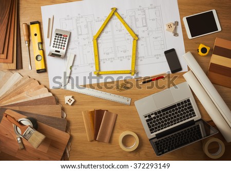 Architect and home interior decorator desktop with tools, laptop, wood swatches and home project draft top view, a meter is composing a house at center