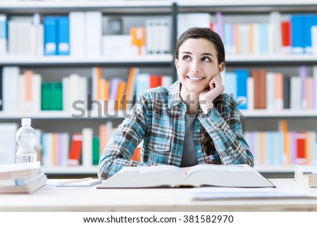 Smiling student girl in the library studying and day dreaming, she is thinking with hand on chin and looking up, education and future concept