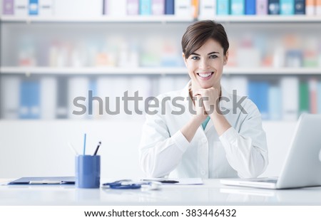 Young female doctor working at office desk and smiling at camera