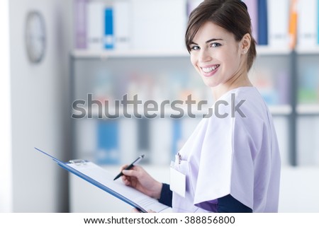 Smiling young female doctor writing a medical report on a clipboard, healthcare professionals