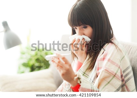 Young sick woman with cold and flu, she is blowing her nose and measuring her body temperature