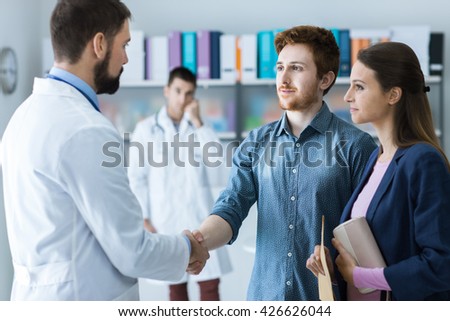 Couple at the doctor\'s office, the doctor is shaking hands with the man, healthcare and consulting concept