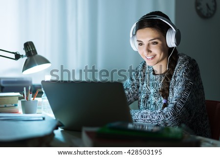 Young attractive woman connecting the internet with a laptop late at night, she is wearing headphones and smiling