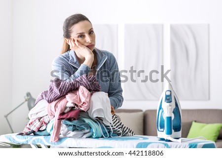 Disappointed unhappy housewife leaning on a pile of laundry on the ironing board