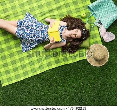Cute girl relaxing outdoors on the grass and reading a novel book, top view