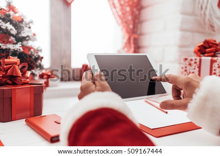 Santa Claus working at desk and using apps on a touch screen tablet, Christmas and technology concept