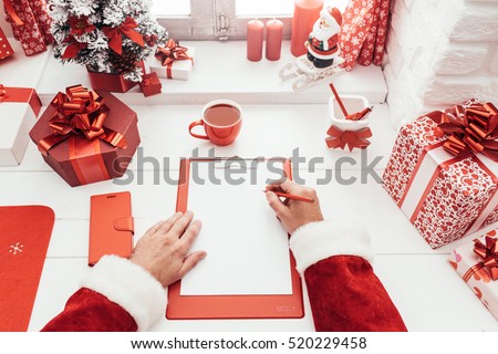Santa Claus working at desk and writing on a blank sheet on a clipboard, he is getting ready for Christmas, point of view shot
