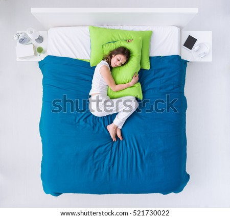 Young woman sleeping in her bedroom, she is curling up on the duvet and hugging a pillow