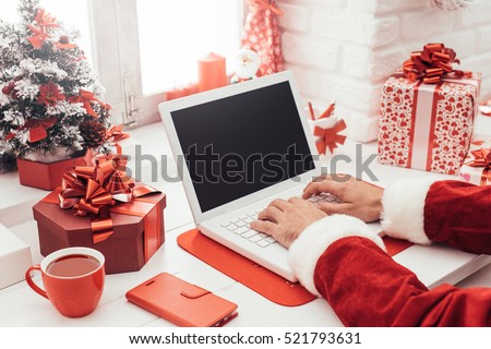 Santa Claus preparing for Christmas and connecting with a laptop, he is working at his desk at home
