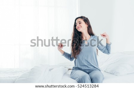 Beautiful woman waking up in her bed in the bedroom, she is stretching and smiling