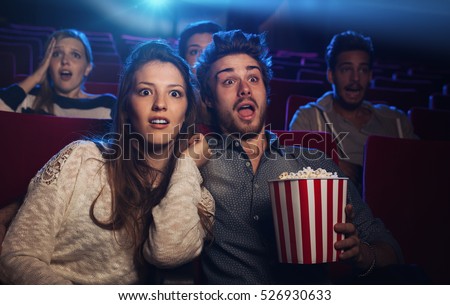 Young teenager couple at the cinema watching an horror movie