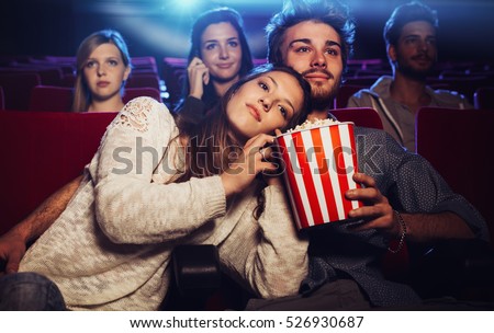 Young loving couple at the cinema watching a movie, she is eating her boyfriend\'s popcorn