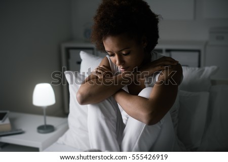 Sad depressed woman sitting in her bed late at night, she is pensive and suffering from insomnia