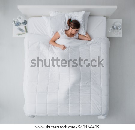Beautiful young woman lying down in bed and sleeping, top view