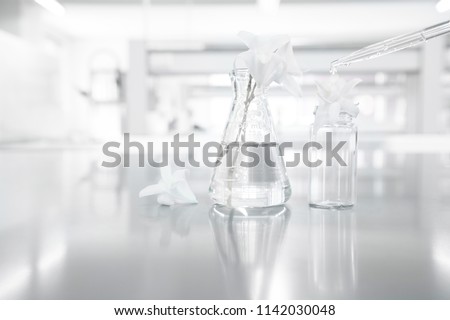 white orchid flower in glass flask with drop of water in cosmetics research science laboratory background