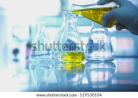 yellow solution in glass flask with scientist hand in research science lab background