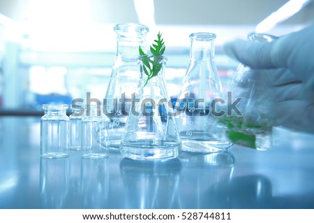 glass flask and bottle with green leaf and hand of scientist shaking liquid  motion background