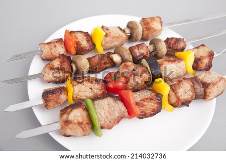 On a white plate kebab, fried pepper and tomatoes.