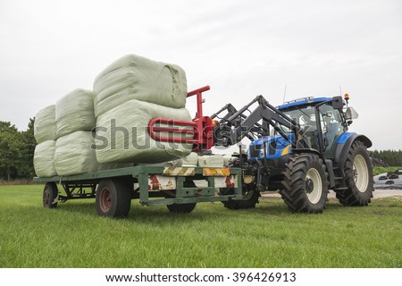 Loading plastic hay bales on a flat cart by a blue tractor