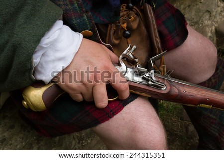 Close up of a flintlock pistol being held naturally resting on knee of a jacobite wearing a kilt