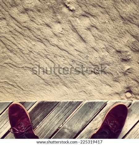 Two feet standing at the edge of sand and a wooden deck.
