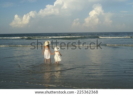 Two little girls with floppy hats standing in the shallow waters of the ocean.