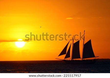 A sail boat against a sky lit in shades of yellow and orange.