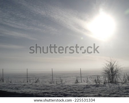 Sun shining over a field and fence covered in snow.