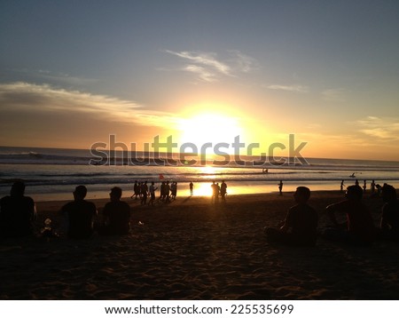A group of people at the beach as the sun sets in the sky.