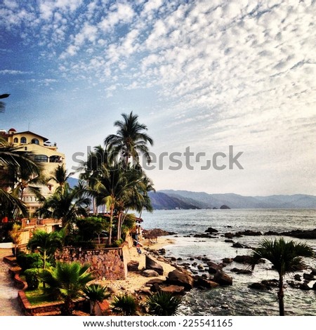 Mediterranean view with palm trees, terraces, mountains and streaky cirrus clouds.