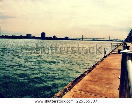 A wooden platform resting above deep blue water in front of a city and long bridge.